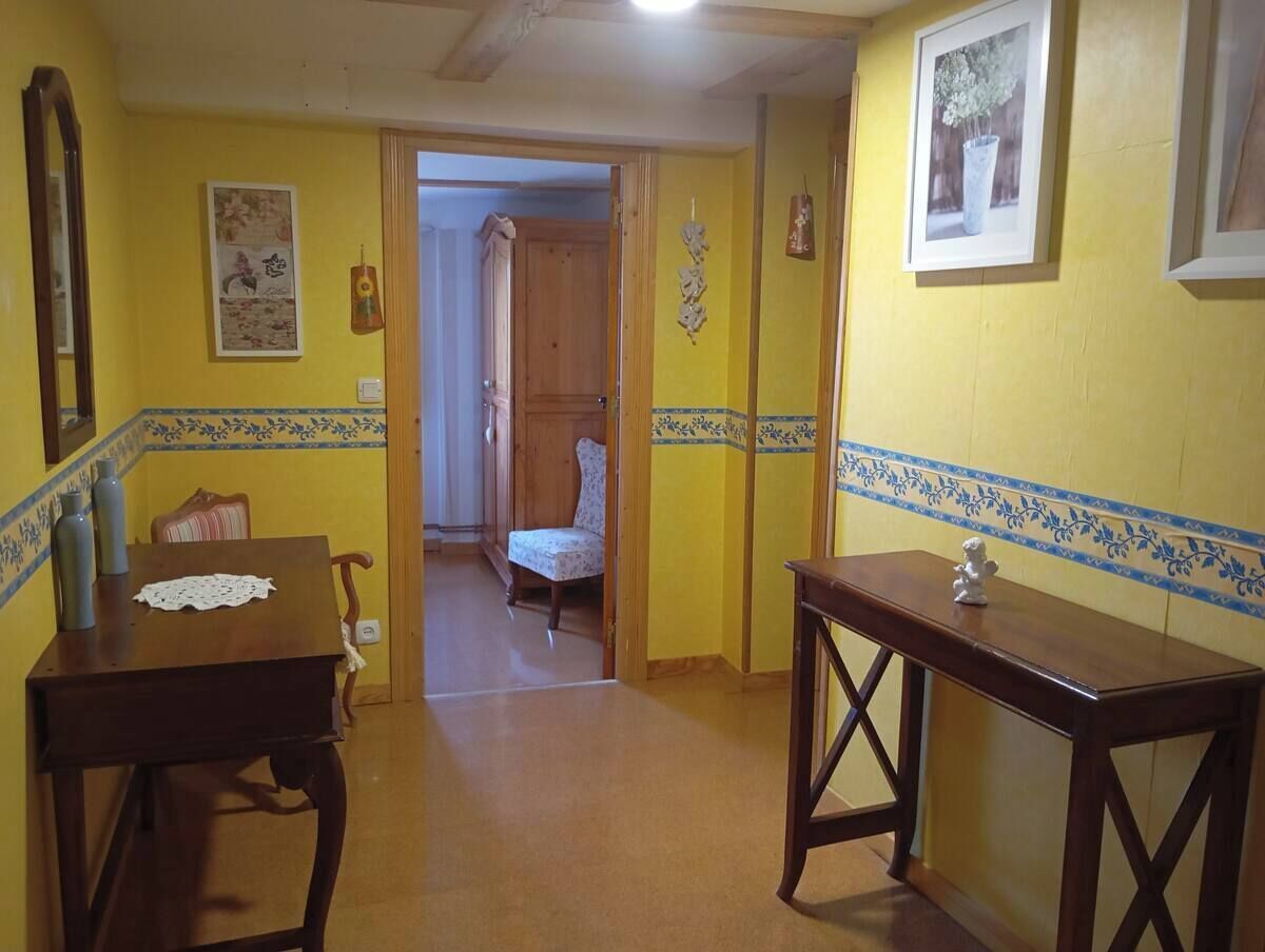 Un pasillo con una mesa de madera, una silla y una mesita con una figurita. Se ve una puerta que da a otra habitación.