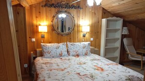 Una habitación con paneles de madera, una cama, dos lámparas fijadas a la pared, un espejo y una silla.