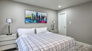 A bedroom with a bed, two bedside tables, a nightstand, a door, and a wall-mounted artwork. - Collins Family-friendly Texas Home With Private Pool (Garland)
