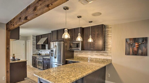 A modern kitchen with dark wood cabinets, granite countertops, stainless steel appliances, and pendant lighting. - Collins Family-friendly Texas Home With Private Pool (Garland)