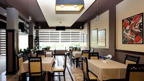 A restaurant with multiple tables and chairs, large windows, and a ceiling light fixture. - Opus Hotel (Berat)