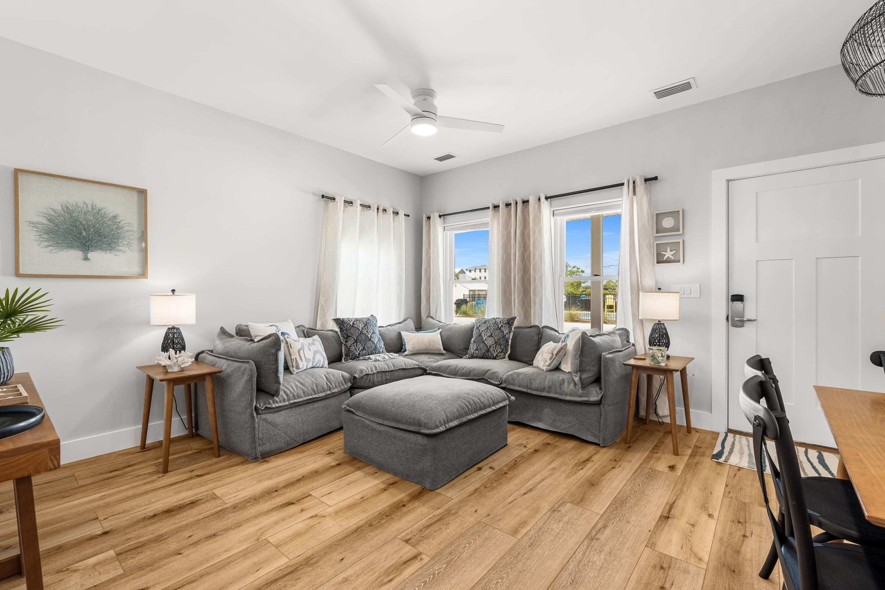 Una sala moderna con un sofá modular, piso de madera y un ventilador de techo.