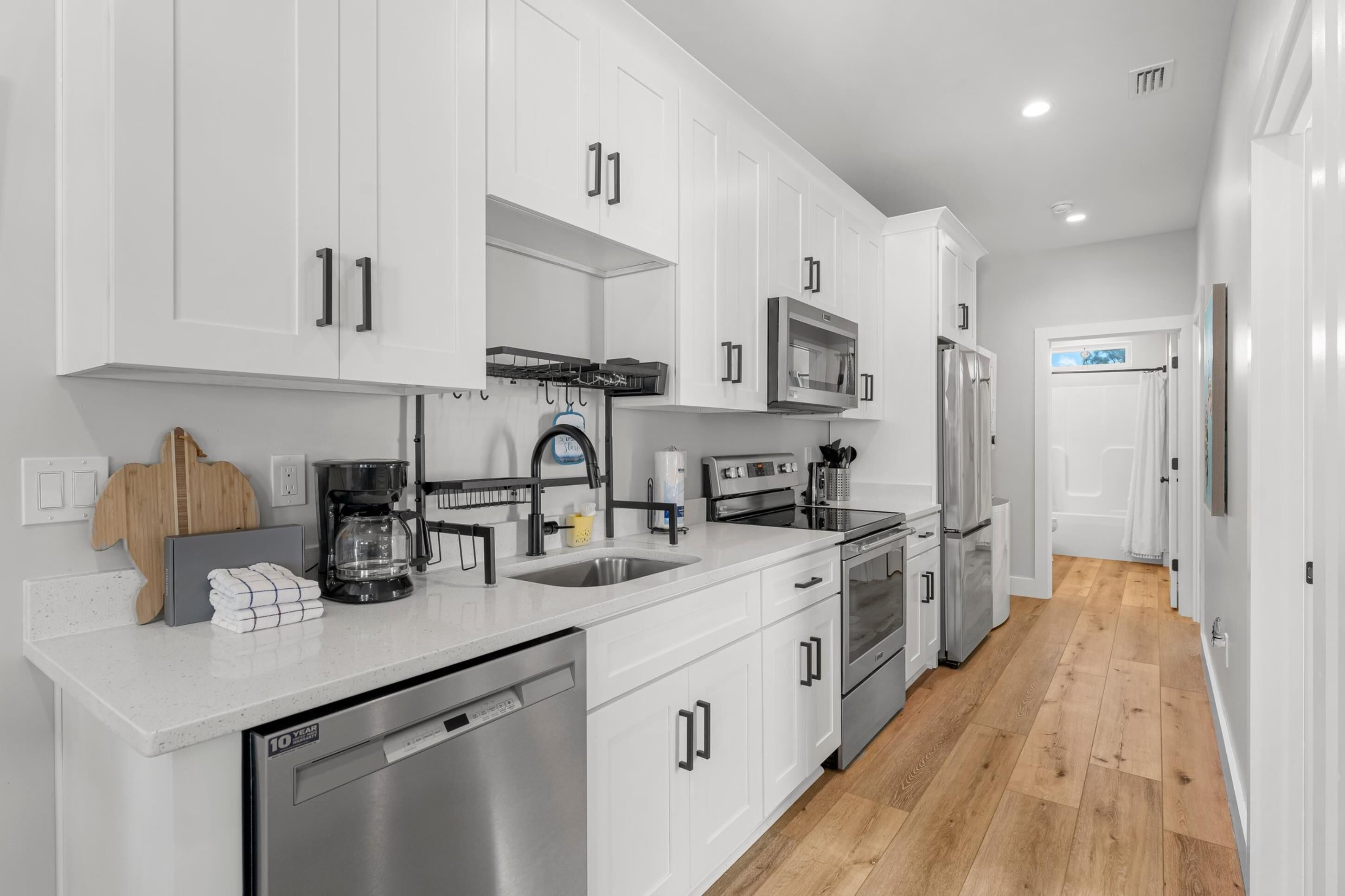 A modern kitchen with white cabinets, stainless steel appliances, and a wooden floor.