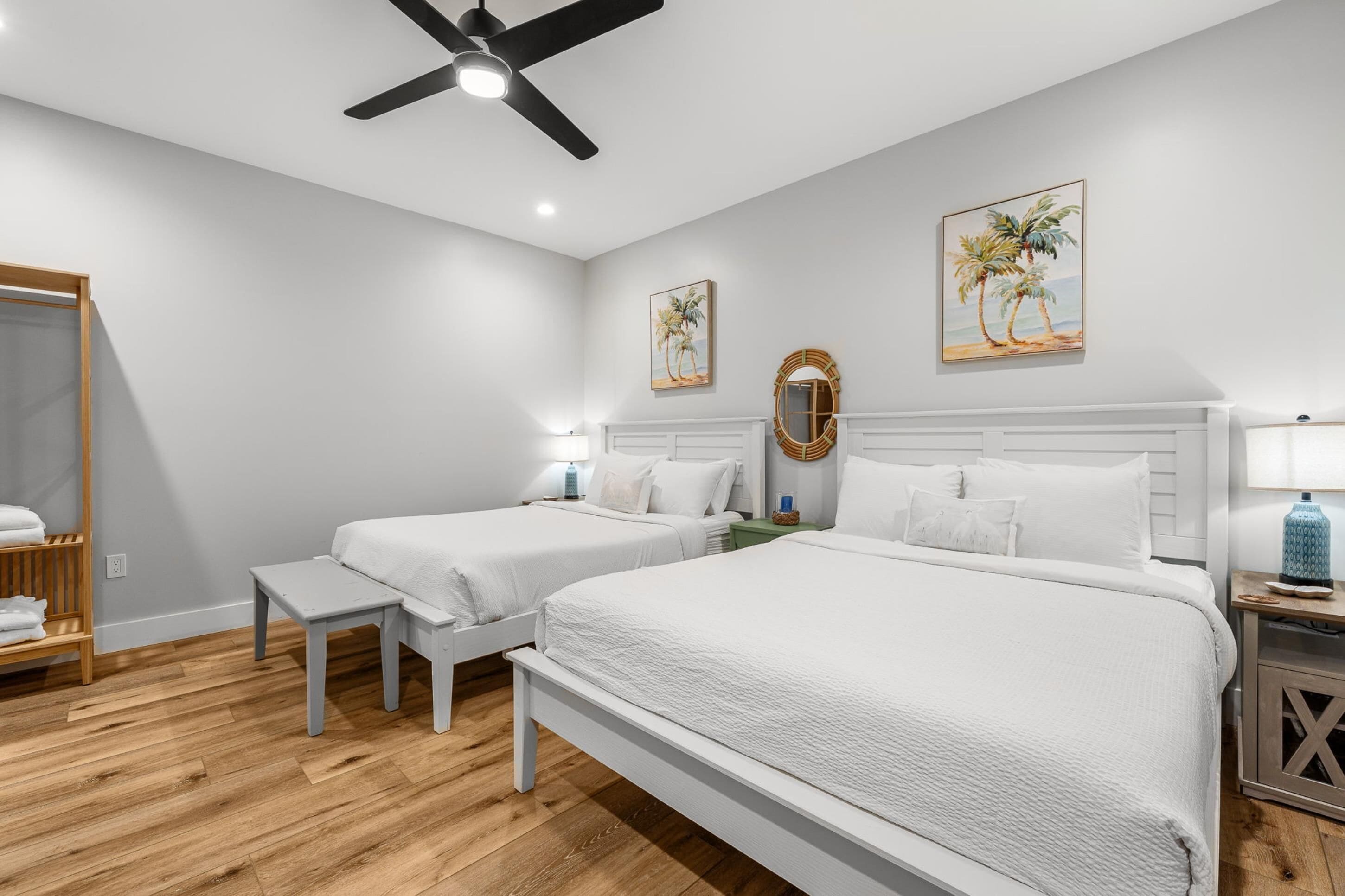 Une chambre d’hôtel avec deux lits, un ventilateur de plafond, un plancher en bois, une armoire et des œuvres d’art accrochées aux murs.