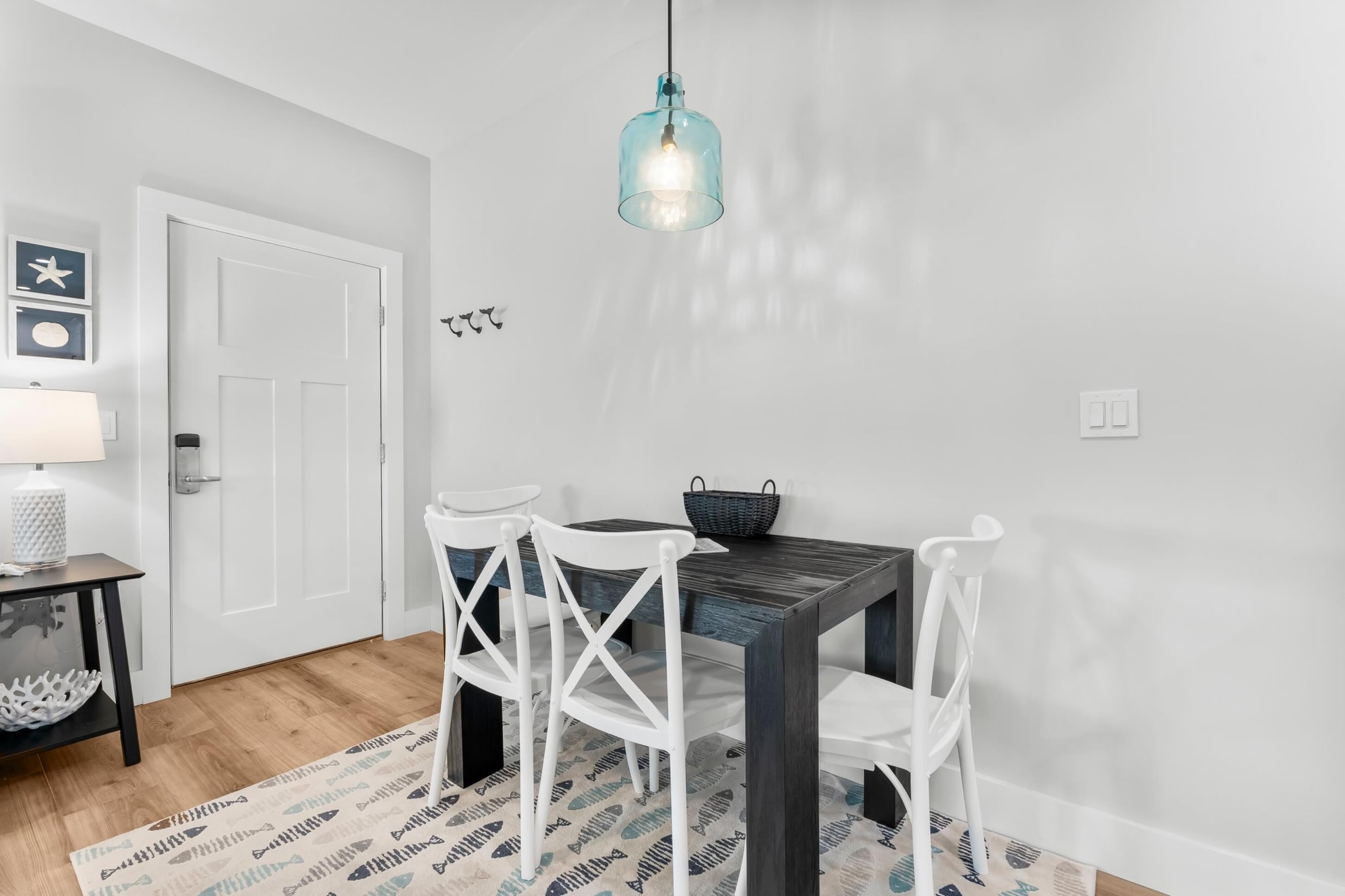 A dining area with a dark wooden table, white chairs, a hanging light fixture, and a patterned rug.