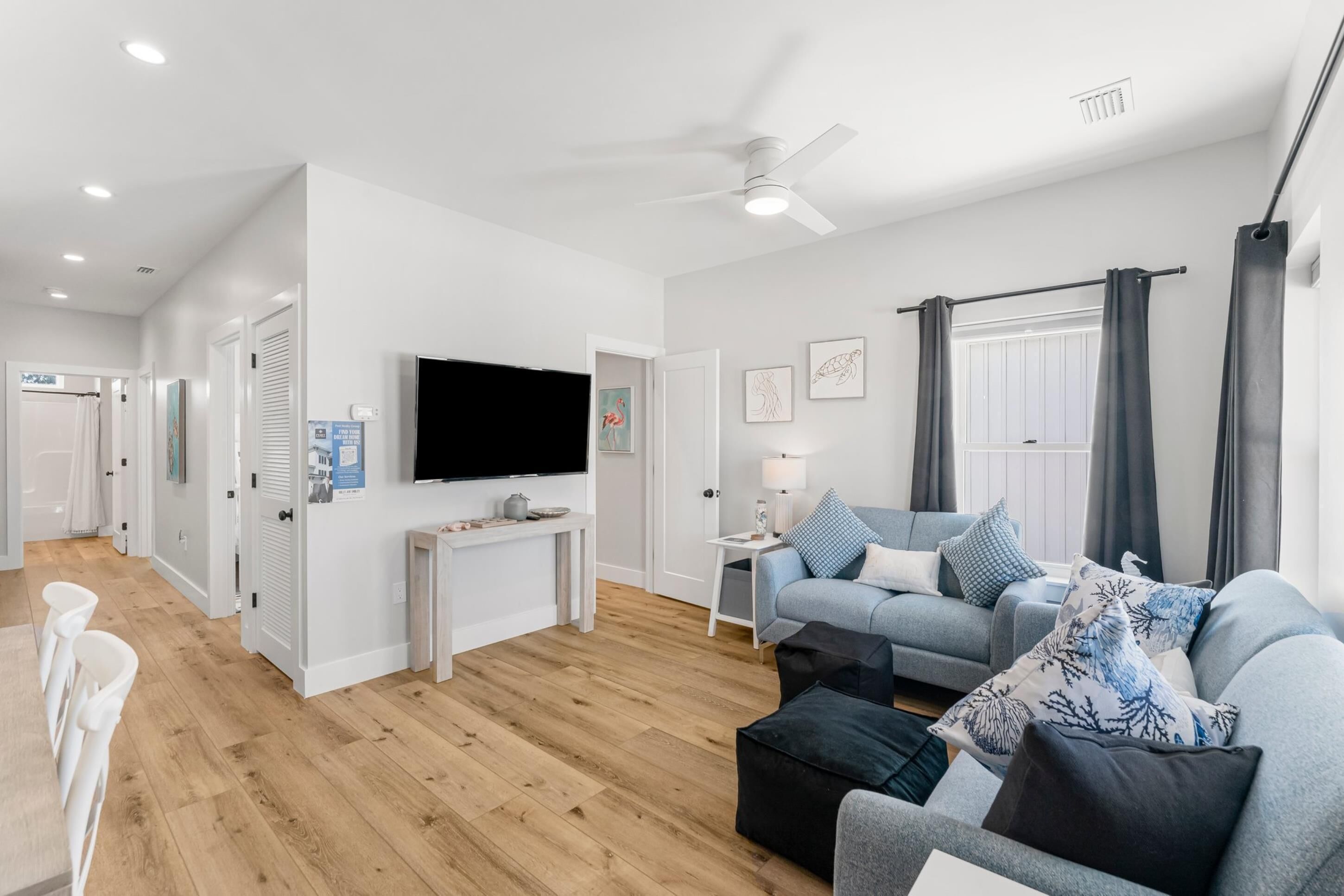 A modern living room with a grey sofa, a flat-screen TV, and a ceiling fan.