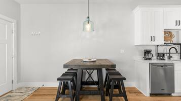 Una cocina moderna con armarios blancos, una mesa de comedor de madera con cuatro taburetes y una lámpara colgante.