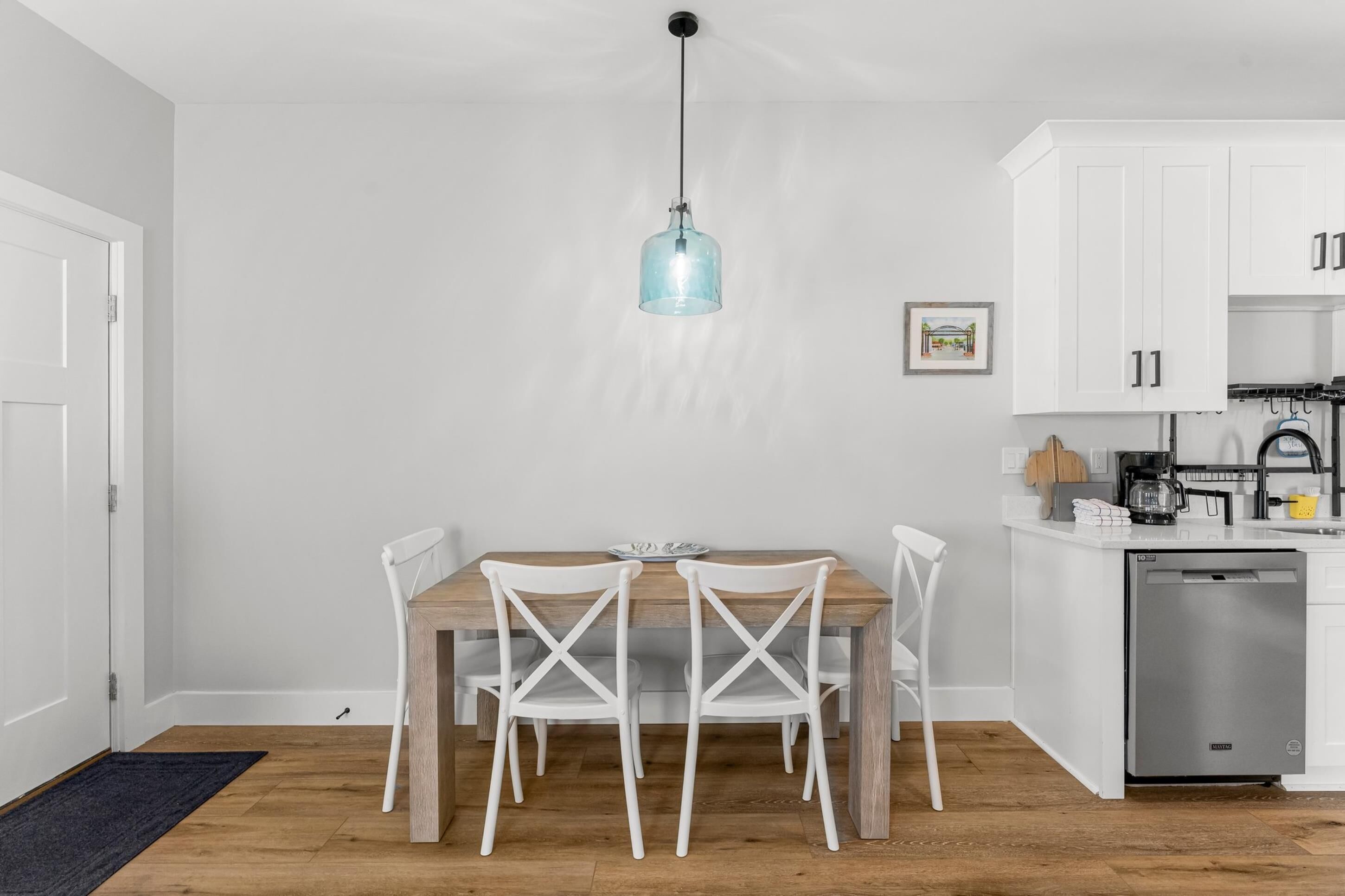 A modern kitchen with white cabinets, a wooden dining table, and a hanging light fixture.