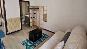 A living room with a sofa, a wooden shelf unit, a radiator, and a patterned rug.