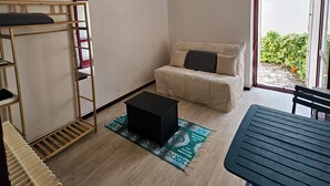 A compact room with a bunk bed, a sofa, a small table, and a view through a glass door.