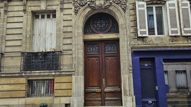 A historic building with a large wooden door, ornate carvings, and a balcony with metal railings.