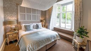 A bedroom with a large bed, a window with curtains, a bedside table with a lamp, and a potted plant. - Forest Side Hotel (Ambleside)