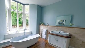 Une salle de bain avec une baignoire sur pieds, un lavabo doté d’un plan de travail en bois et une fenêtre donnant sur un paysage verdoyant.
