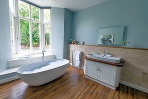A bathroom with a freestanding bathtub, a sink with a wooden countertop, and a window with a view of greenery. - Forest Side Hotel (Ambleside)