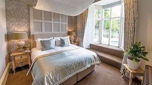 A bedroom with a large bed, a window with curtains, a bedside table with a lamp, and a potted plant. - Forest Side Hotel (Ambleside)