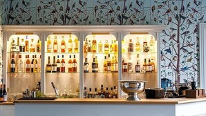 A bar with shelves of liquor bottles, a bar counter, and a decorative bird mural on the wall. - Forest Side Hotel (Ambleside)