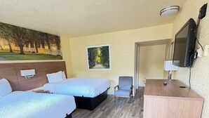 A hotel room with two beds, a desk, a chair, a TV, and a painting on the wall. - University Inn Gainesville (Gainesville)
