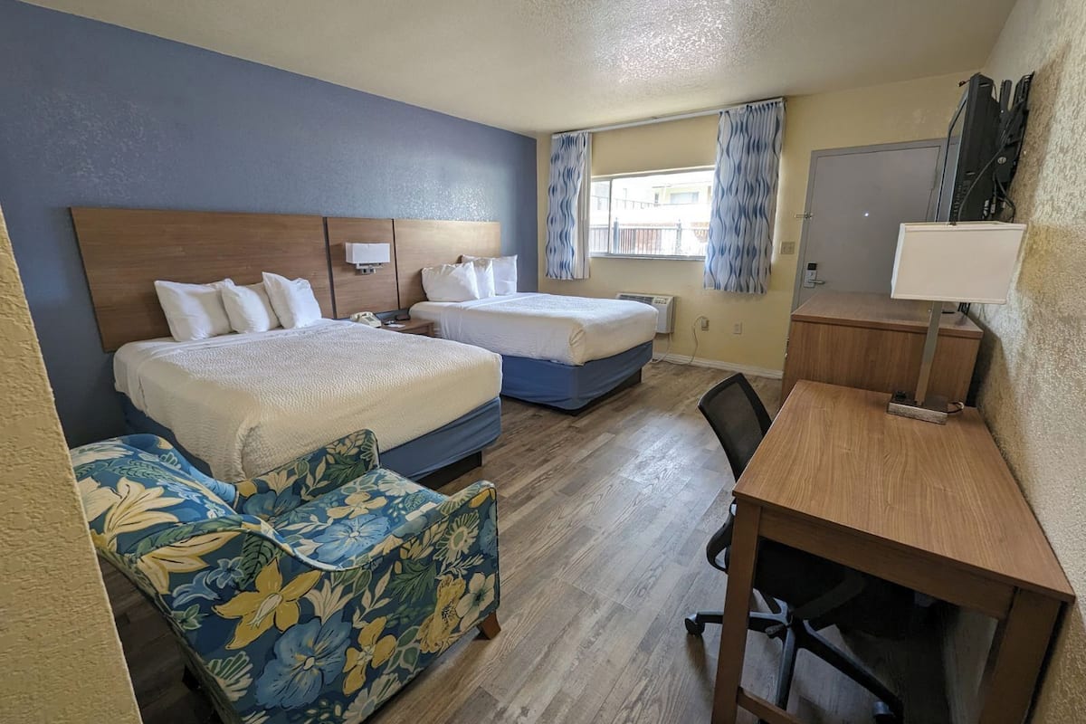 Ein Hotelzimmer mit zwei Betten, einem Schreibtisch, einem Stuhl und einer kleinen Sitzecke.