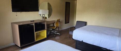 A hotel room with two beds, a desk with a chair, a television, and a mirror.