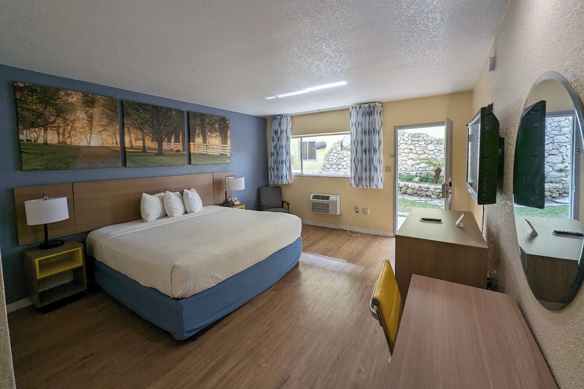 Ein Hotelzimmer mit einem großen Bett, einem Schreibtisch, einem Stuhl, einem Fernseher und einem Fenster mit Vorhängen.