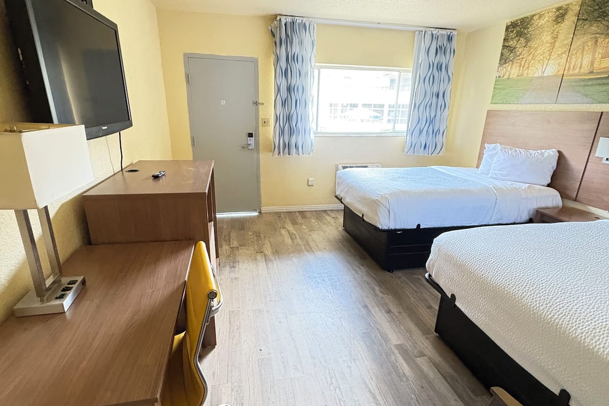 Ein Hotelzimmer mit Bett, Schreibtisch, Stuhl, Fernseher und einem Fenster mit Vorhängen.