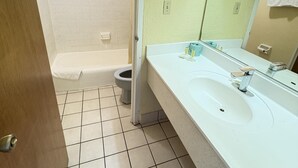A bathroom with a white sink, a mirror, and a shower area. - University Inn Gainesville (Gainesville)
