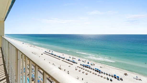 A beach view from a balcony with a clear sky, a sandy beach, and umbrellas. - Fall Deals + Snowbird Rates | Gulf Front Beach Escape (Panama City Beach)