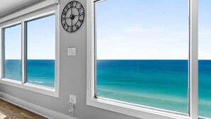 A room with large windows overlooking a turquoise ocean, a wall-mounted clock, and a power outlet. - Fall Deals + Snowbird Rates | Gulf Front Beach Escape (Panama City Beach)