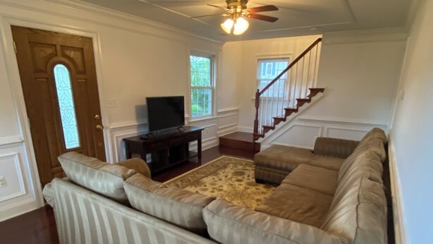 A living room with a large striped sofa, a television on a stand, a staircase, and a ceiling fan.