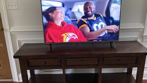 A television on a wooden TV stand with three drawers.