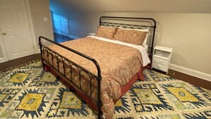 A bedroom with a metal bed frame, a patterned bedspread, a bedside table, and a patterned rug.