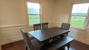 A dining room with a rectangular table, four chairs, and two windows with a view of a green landscape.