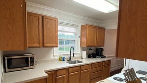 A kitchen with wooden cabinets, a microwave, a sink, a coffee maker, and a knife block.