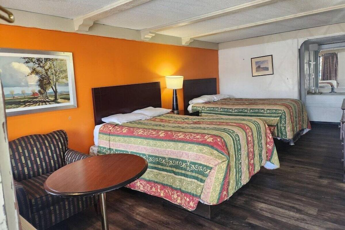 A hotel room with two beds, a small table, a sofa, and a painting on the wall.