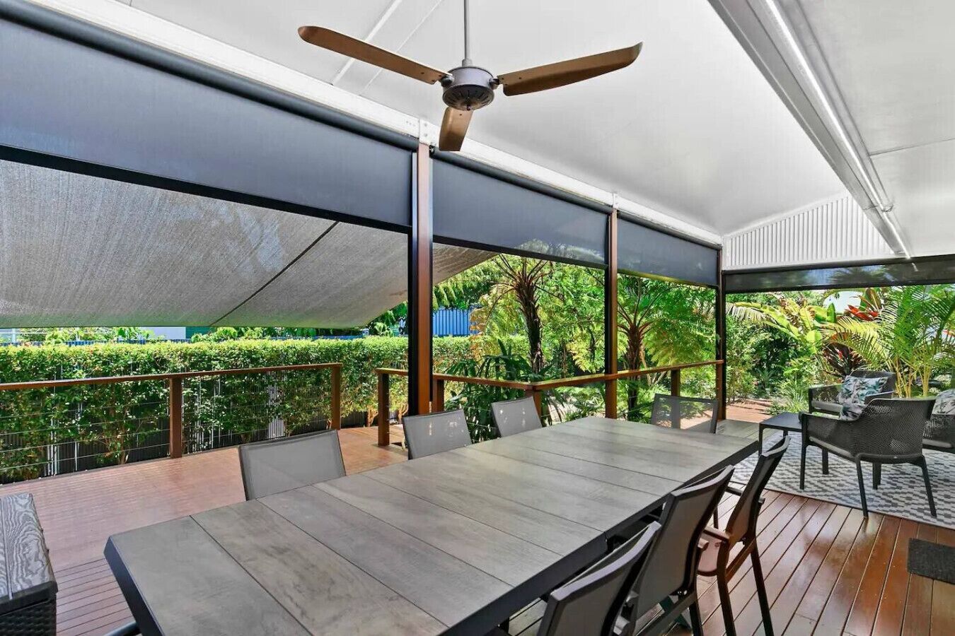 Un espace de restauration en plein air avec une table et des chaises, un ventilateur de plafond et une vue sur un jardin luxuriant.