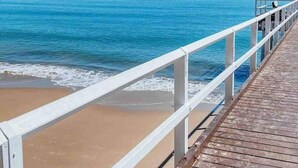 A wooden pier leading to a sandy beach with clear blue water and a distant landmass. - Family Friendly Walk to Beach Tropical Retreat + BBQ Deck (Point Vernon)