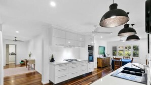 A modern kitchen with white cabinetry, a central island, and pendant lighting. - Family Friendly Walk to Beach Tropical Retreat + BBQ Deck (Point Vernon)