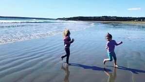 Dos niños jugando en una playa con cielo despejado.