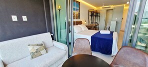 Una habitación de hotel con sofá, una cama con colcha azul, una silla y una mesita.