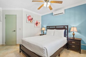 A bedroom with a bed, two bedside tables with lamps, a ceiling fan, and a door.