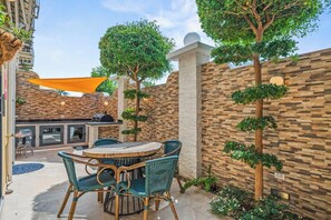 An outdoor patio with a round table and chairs, a barbecue grill, and a stone wall. - 2BR Home w/ Outdoor Kitchen & Shared Pool (Noord)