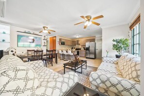 A modern living room with a sofa set, a dining area, and a kitchen in the background.