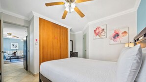 A bedroom with a bed, wooden wardrobe, ceiling fan, and artwork on the wall.