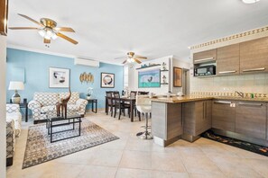 A modern living room with a sofa, coffee table, and a TV. There is a kitchen with a microwave and cabinets. - 2BR Home w/ Outdoor Kitchen & Shared Pool (Noord)