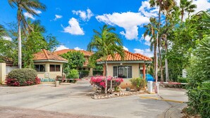 A gated residential area with a small building, palm trees, and a clear sky.