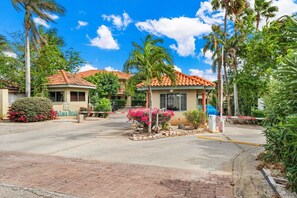 A gated residential area with a small building, palm trees, and a clear sky. - Charming 2BR Home • Outdoor Kitchen (Noord)