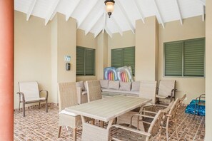 Ein überdachter Außenbereich mit Tisch, Stühlen und einer Couch, ausgestattet mit einem Deckenventilator.