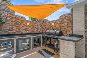 Ein Outdoor-Kochbereich mit Grill, einer Bar und einem Baldachin.