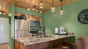 A kitchen with a granite countertop, stainless steel appliances, and wooden cabinets. There are two bar stools and a coffee maker on the counter. - Ozark Mountain Lake Home (Branson West)