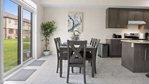 Une cuisine moderne avec des meubles de couleur sombre, un coin repas comprenant une table et des chaises, et une grande fenêtre donnant sur une pelouse verdoyante.